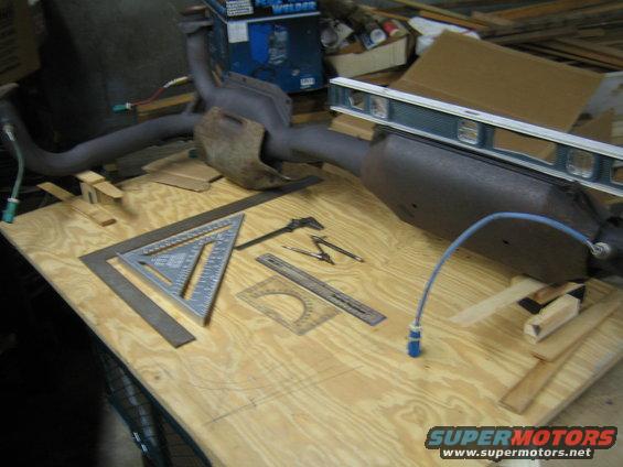 Exhaust pipe and muffler assembly on a wooden workbench with measuring tools