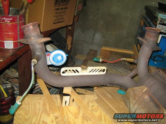 exhaust pipe with oxygen sensors attached, resting on wood