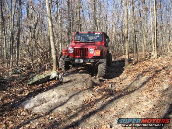 Red Jeep Wrangler TJ navigating a rocky forest trail