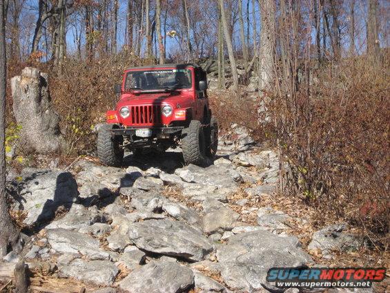 Red Jeep Wrangler with lifted suspension and large tires on a rocky trail