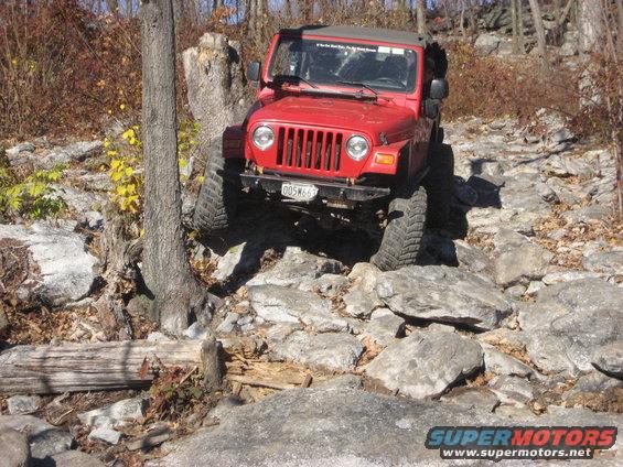 Red Jeep Wrangler navigating a rocky trail, front grille visible