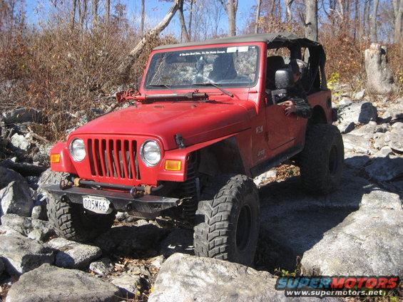 Red Jeep Wrangler TJ with aftermarket bumper and large tires navigating rocks