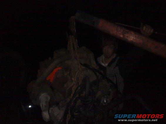 Engine being lifted by a crane with a person standing nearby in the dark