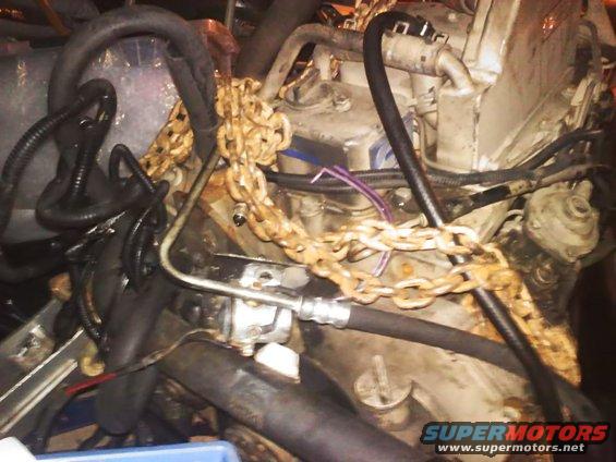 Engine block with rusty chains draped over it, hoses, and wiring