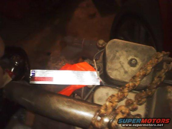 Engine component with a thick chain wrapped around it. A white label with red and blue text is visible