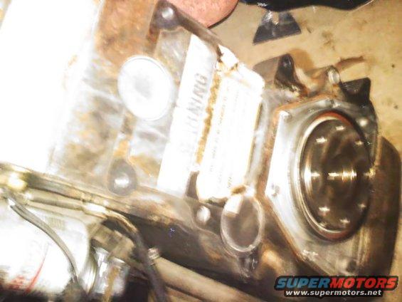 Engine part with a "WARNING" label attached. It has a circular metal plate with bolts