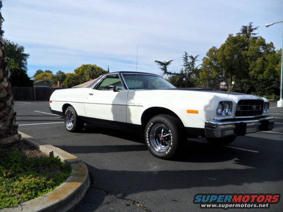 White Ford Ranchero parked in a lot, black hood accent, chrome wheels, Goodyear tires