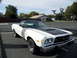 1973 Ford Ranchero - A white 1973 Ford Ranchero with a black hood stripe and vinyl top is parked in an empty lot.