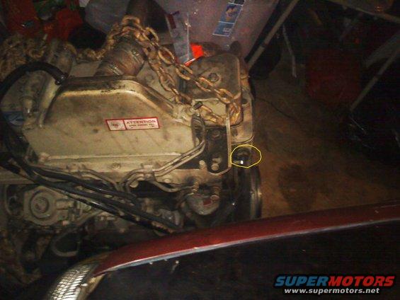 Engine block with chain and hoses, red car hood in foreground