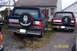 1996 Ford Bronco - Rear view of two Ford Broncos, one blue and silver, the other red, parked outdoors.