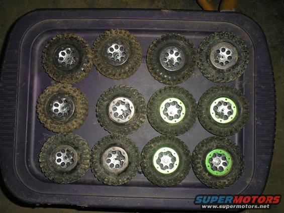 Twelve RC car tires with silver rims and knobby treads, some with green accents, laid out on a purple tray