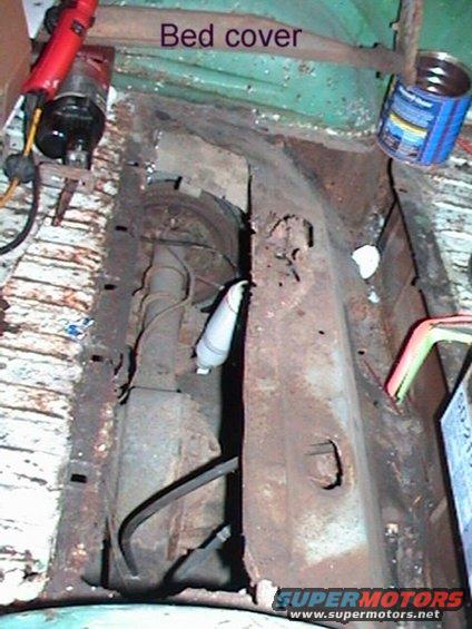 Rusted vehicle bed interior with exposed drivetrain components and a can of paint