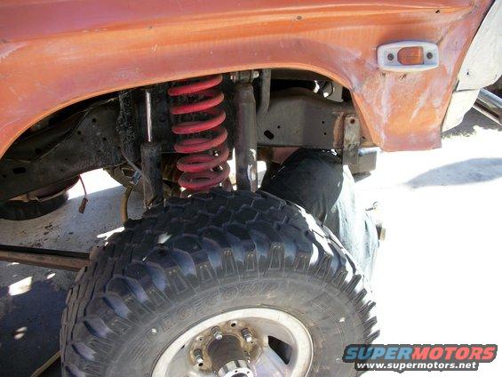 Close-up of orange truck's front suspension with red coil springs and large tire