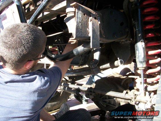 Man in blue shirt working on the suspension of a vehicle, showing the differential and red coil springs