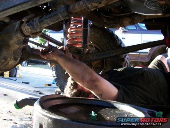 Underneath view of 1969 Ford F-250 being repaired, with mechanic working on suspension