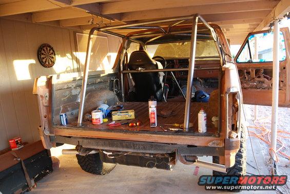 Pickup truck bed with custom roll cage installed, interior visible. Tools and cans on the bed floor