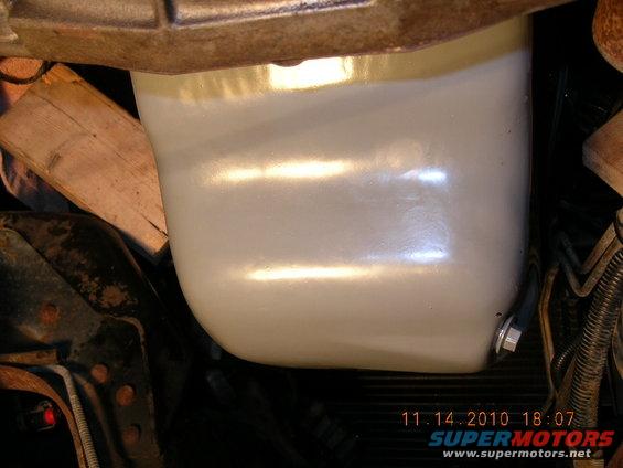 Close-up of a vehicle's oil pan, possibly recently painted or cleaned. Some wooden blocks are visible nearby