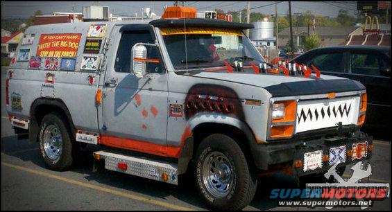 Gray pickup truck with orange trim, custom shark teeth grille, and various stickers