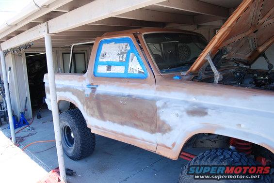 Rusty brown SUV with hood open, windows taped, and bodywork in progress