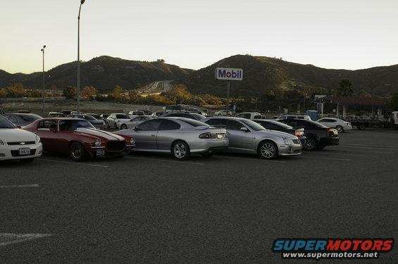 Cars parked in a lot with a Mobil sign and mountains in the background