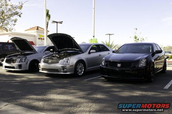 Three Cadillac sedans parked in a lot, two with hoods open. Black Cadillac in foreground