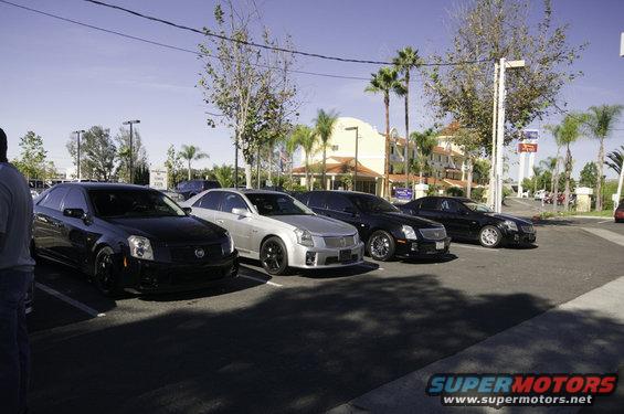 Four Cadillacs parked in a lot. The silver one is a CTS, and the black ones look like CTS models too