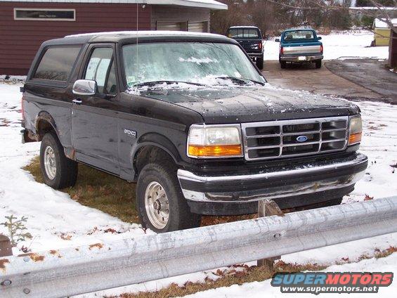 Black 1996 Ford Bronco parked in snow with two pickup trucks in the background