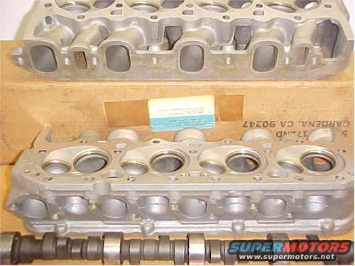 Two aluminum engine cylinder heads and a camshaft with a box and label