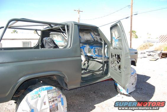Ford Bronco with doors open, interior taped off for paint, roll cage installed, wheels covered