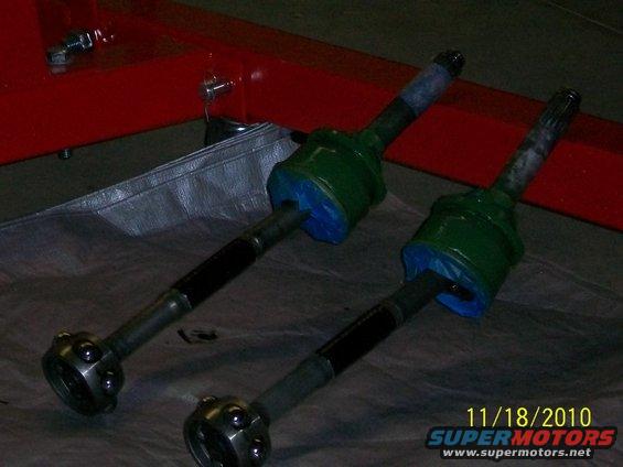 Two green CV axles with blue protective covers on a gray tarp