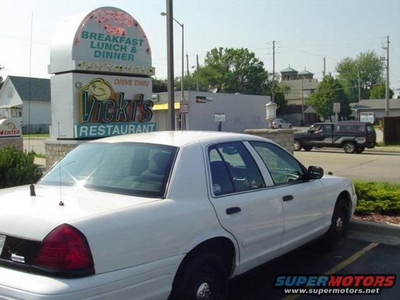 White 2003 Ford Crown Victoria parked near Vicki's Restaurant. A black pickup truck is visible in the background
