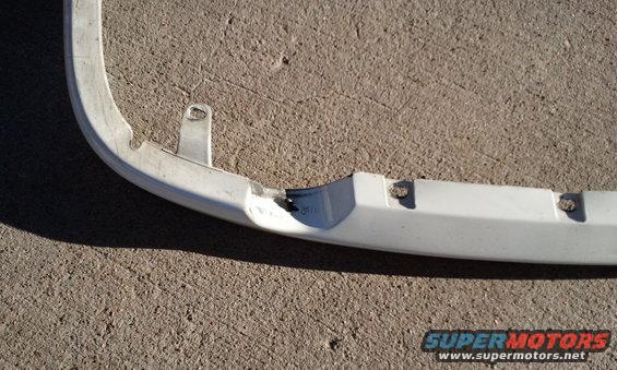 Close-up of a white car bumper section with damage and mounting points