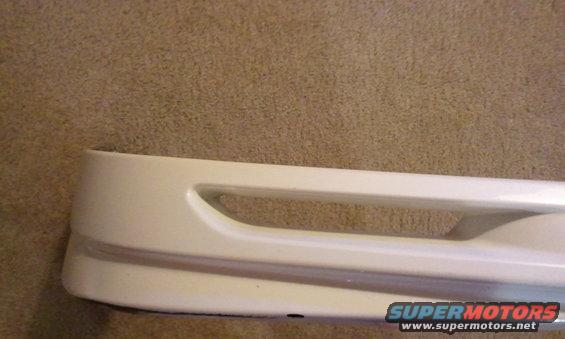 White car bumper with a horizontal cutout, resting on a carpeted surface