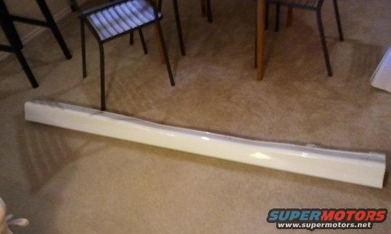 White car side skirt on carpeted floor, with chairs and table legs in background