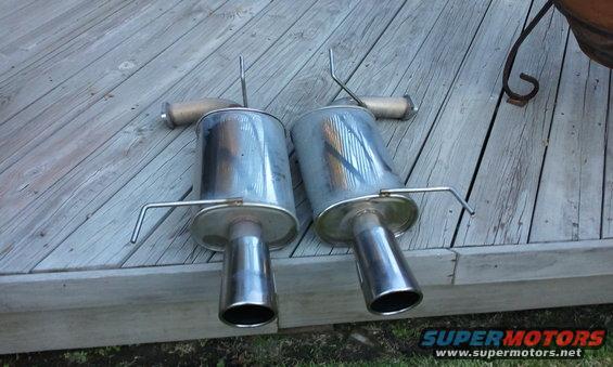 Two chrome exhaust mufflers with bent hangers on a wooden deck