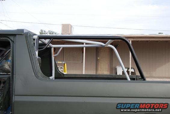 Side view of a gray Ford Bronco with a white and black roll cage installed in the interior and bed
