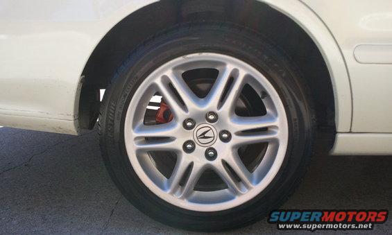 White car's front wheel with silver 5-spoke rim and Acura logo, red brake caliper visible. Side panel and fender shown