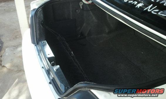 Open car trunk interior with black carpet and a cargo net, white exterior visible