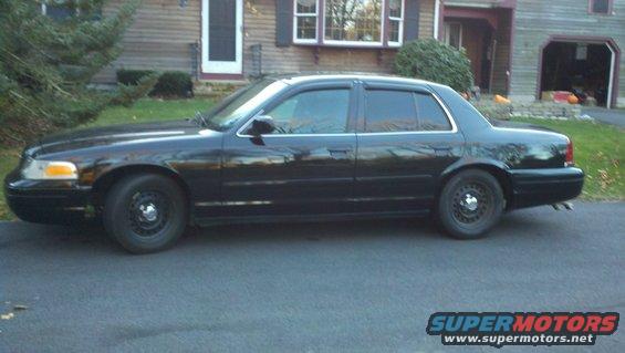 Side view of a black sedan with tinted windows and steel wheels parked in front of a house