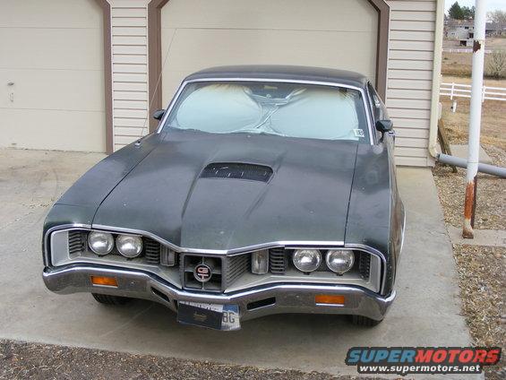 Front view of a dark green 1970 Oldsmobile 442 with a hood scoop and sunshades in the windshield
