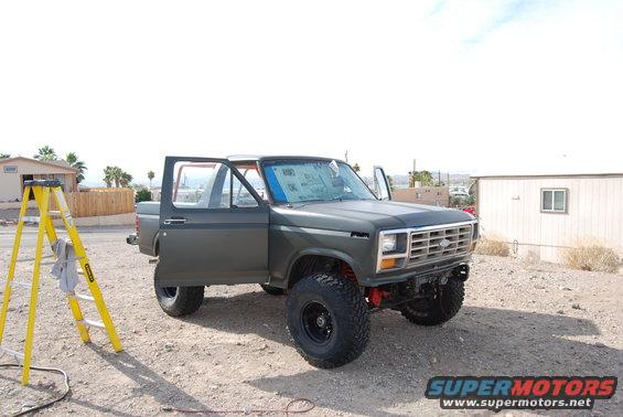 Dark green Ford Bronco with doors open, parked on gravel. Yellow ladder to the left