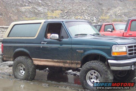 Dark green Ford Bronco with tan trim, lifted, off-road tires, stuck in mud