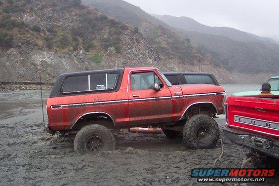 Red lifted SUV stuck in mud next to a red Ford pickup truck
