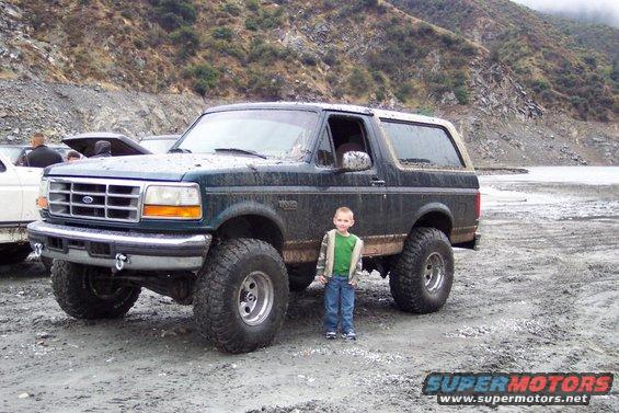 Dark green Ford Bronco with lifted suspension and large tires, parked on a dirt road