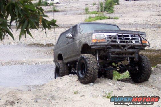 Mud-covered SUV with lifted suspension and off-road tires navigating a dirt and water terrain