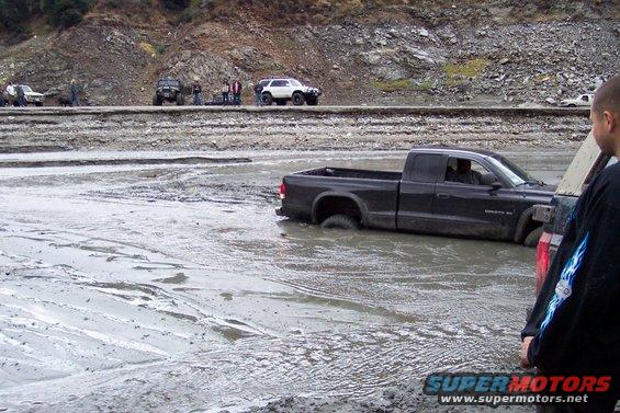 Black pickup truck stuck in mud, rear passenger side wheel submerged