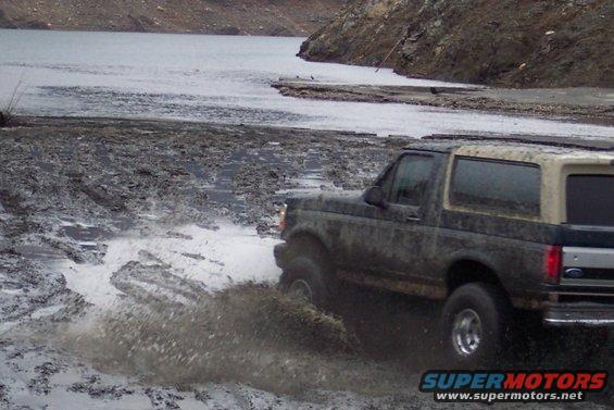 Muddy 1995 Ford Bronco driving through water, 3q-front view