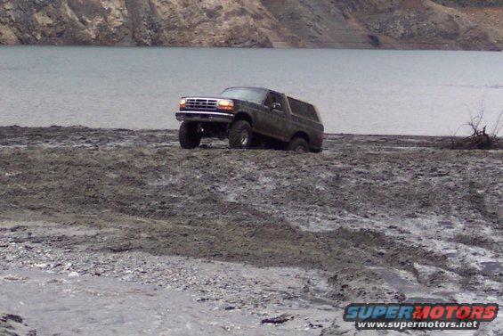 1995 Ford Bronco driving on muddy bank with water in background