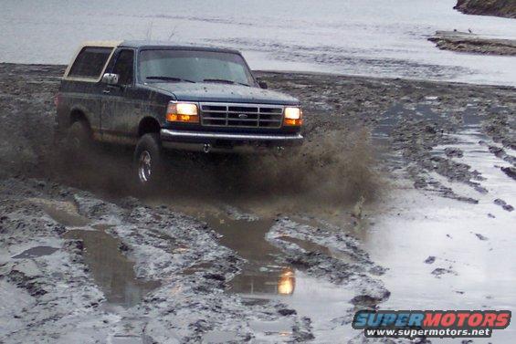 Dark blue Ford Bronco driving through a muddy area, splashing water