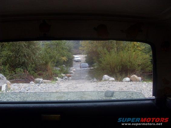 View from inside a vehicle looking out at two SUVs on a dirt road
